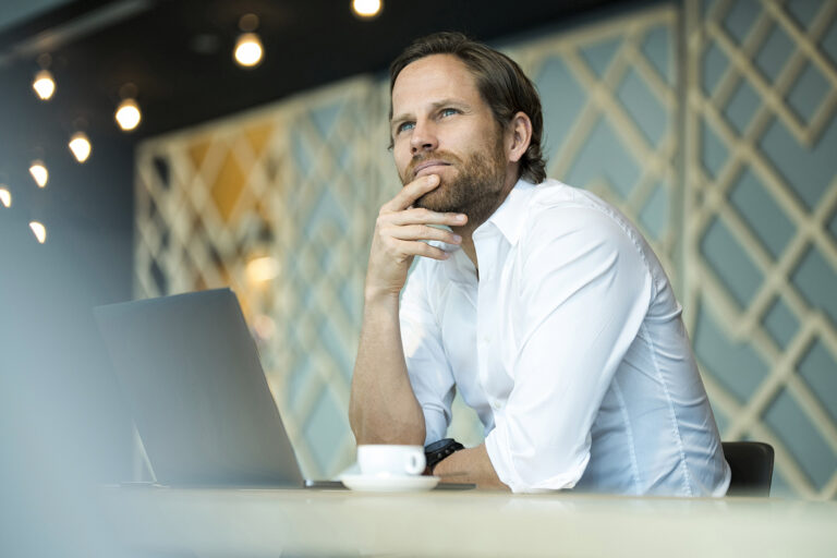 Casual pensative entrepreneur working on laptop in office lounge
